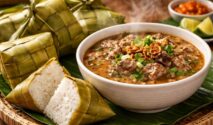 Sajian otentik Coto Makassar dengan pendamping wajib ketupat daun pandan yang wangi dan kenyal di atas meja kayu tradisional.