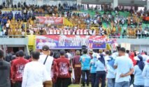Pemandangan dari belakang kerumunan besar penonton yang berdiri di tribun stadion sepak bola yang penuh di Bone, dengan spanduk "RISE OF CHAMPIONS" di latar belakang.
