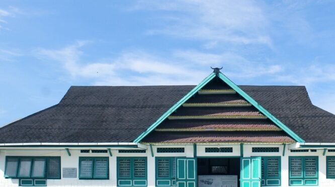 Fasad depan bangunan Museum La Pawawoi Bone dengan arsitektur tradisional atap pelana bertumpuk dan ornamen kepala kerbau di puncaknya, di bawah langit biru berawan.