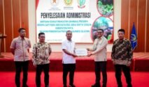 Sesi foto bersama di panggung Aula Asta Cita berlatar layar digital besar bertuliskan "PENYELESAIAN ADMINISTRASI BANTUAN KEMASYARAKATAN (BANMAS) PRESIDEN BERUPA SAPI". Lima orang pria berdiri berjejer mengenakan pakaian batik dan kemeja rapi, di mana dua orang di antaranya yang berada di tengah sedang memegang map dokumen serah terima sapi kurban bantuan Presiden.