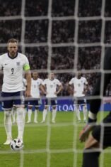 Harry Kane mengenakan seragam Timnas Inggris bersiap mengambil tendangan penalti dengan sudut pandang dari belakang gawang lawan di stadion sepak bola.