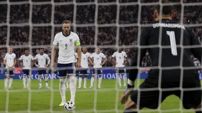 Harry Kane mengenakan seragam Timnas Inggris bersiap mengambil tendangan penalti dengan sudut pandang dari belakang gawang lawan di stadion sepak bola.